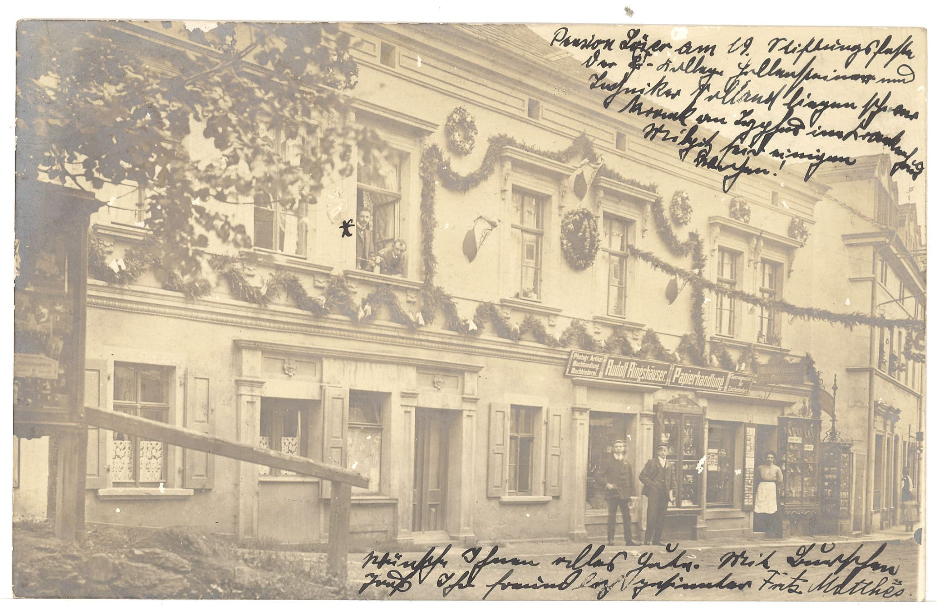 Historische Fotopostkarte: das festlich geschmückte Haus mit Papierhandlung im Erdgeschoss